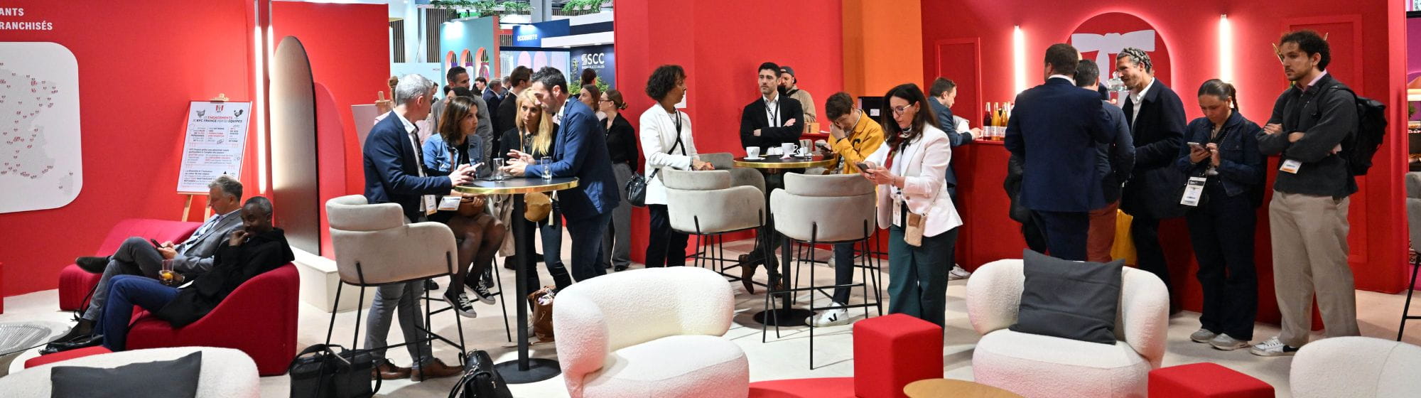 Professionals gathered in a welcoming and modern lounge area at a B2B trade show, networking at high tables. 