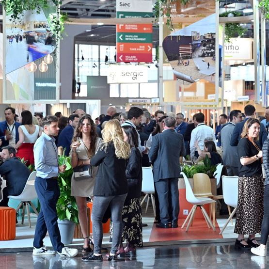 A lively networking area at the Siec trade show, with numerous professionals engaging in discussions in a modern and friendly atmosphere. Visitors are seen chatting in small groups, holding drinks and promotional items. The setting is decorated with plants and directional signs indicating various event zones.