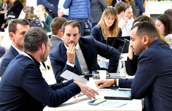 Group of professionals engaged in a business meeting at a trade show, with laptops and tablets on the table.