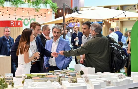 Group of professionals discussing an architectural model at a trade show, in a dynamic networking space.